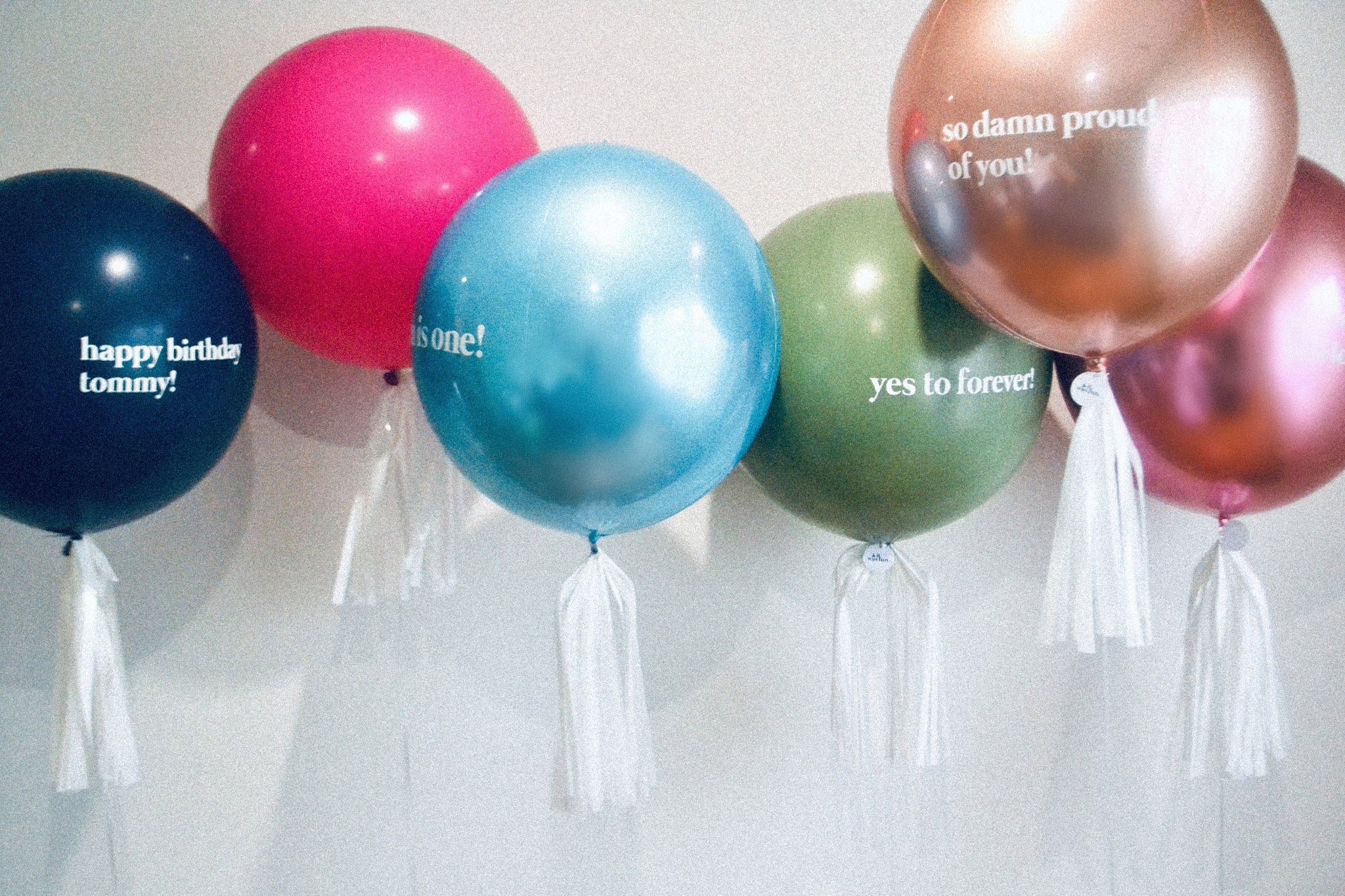 group of personalised balloons with custom text all floating in front of a white wall